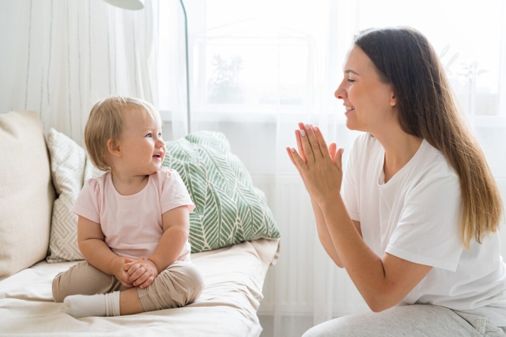 Smiling mother clapping and looking at happy toddler sitting on couch in living room.jpg